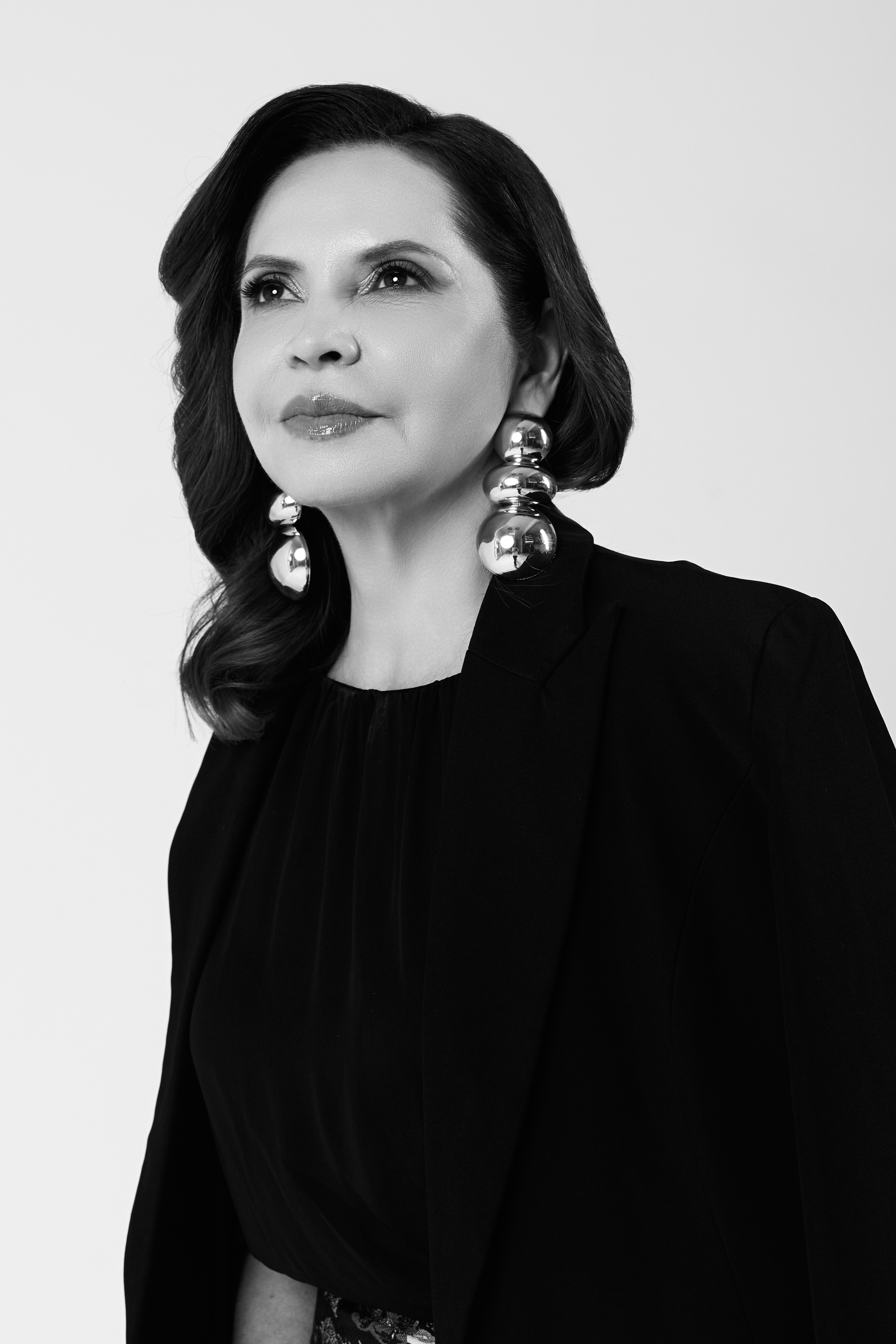 Woman with dark hair wearing large earrings and a black outfit, looking to the side.