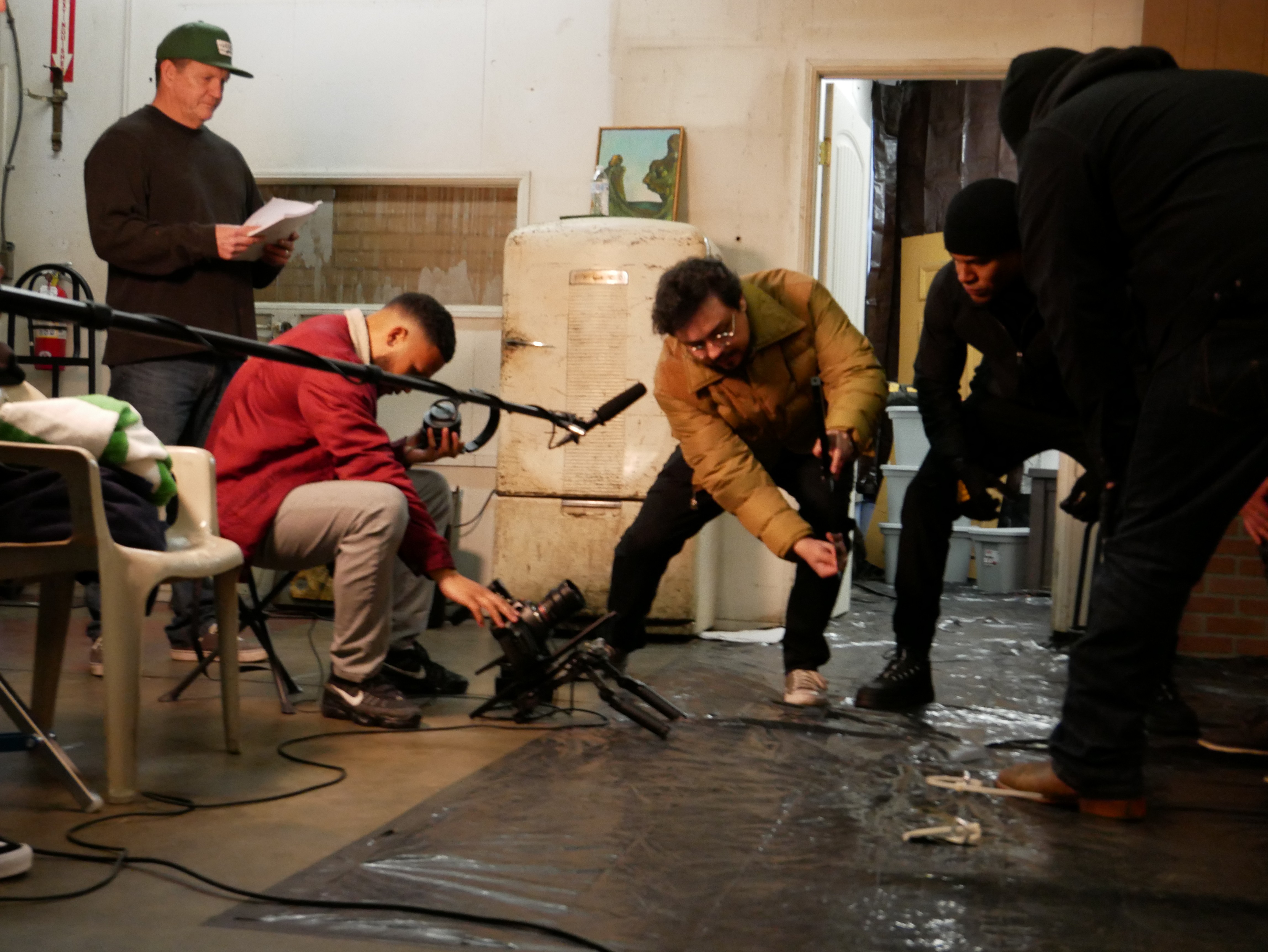Group of people working on a film set, with equipment and a person holding a script, in an indoor space.