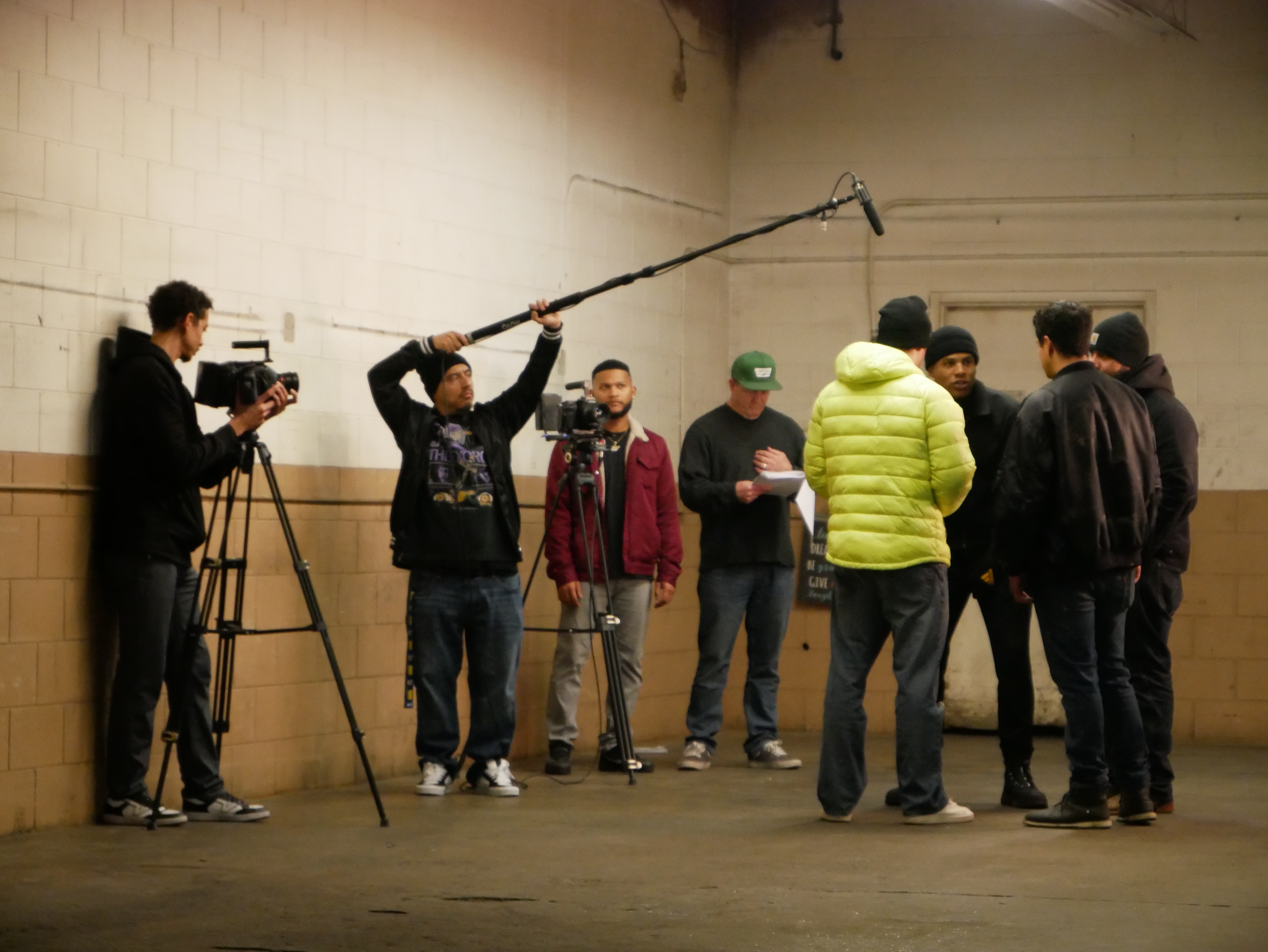 Group of people, some with notebooks, in an indoor space with a camera operator filming them.