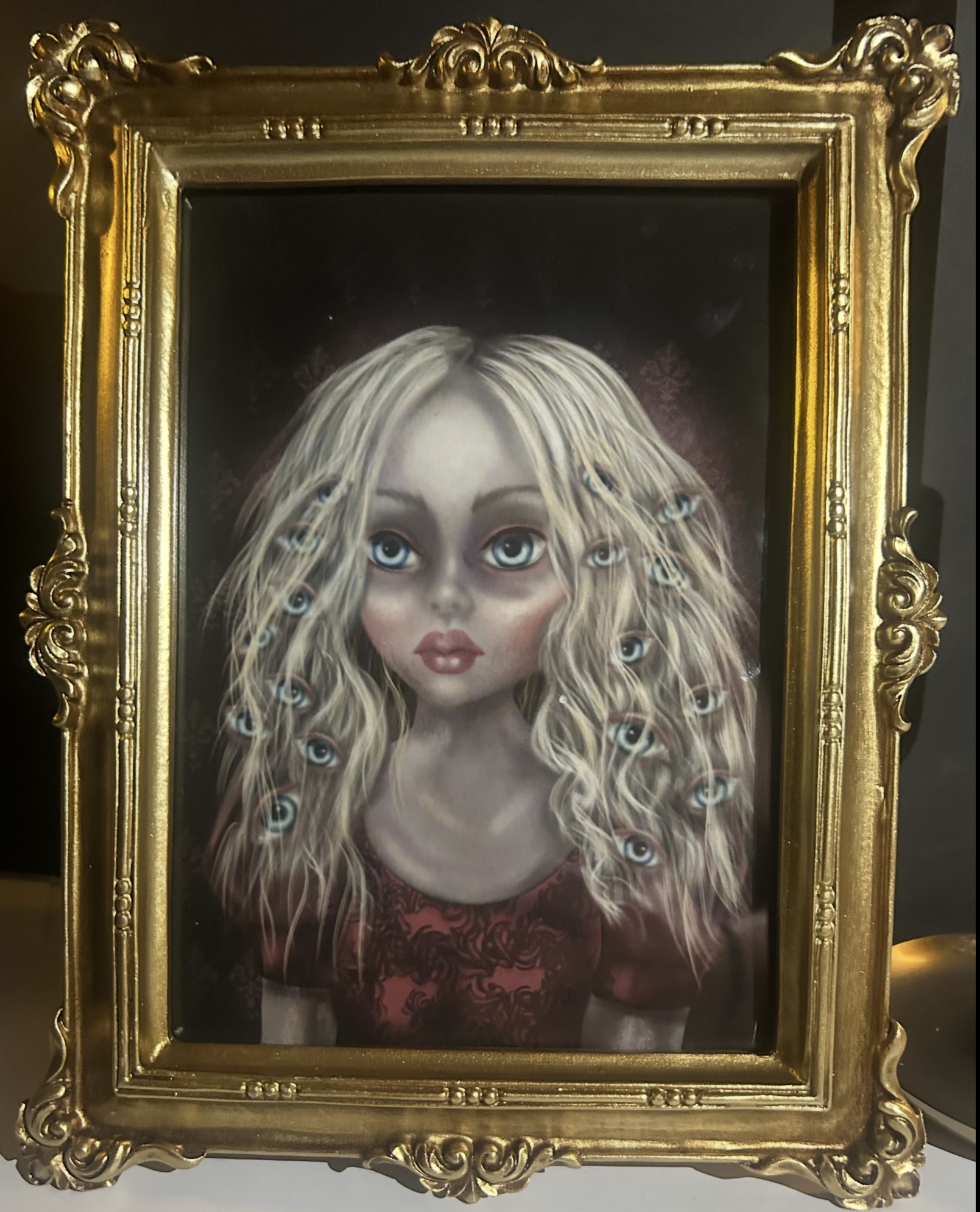 Portrait of a girl with long, curly blonde hair and large eyes, in a decorative gold frame.