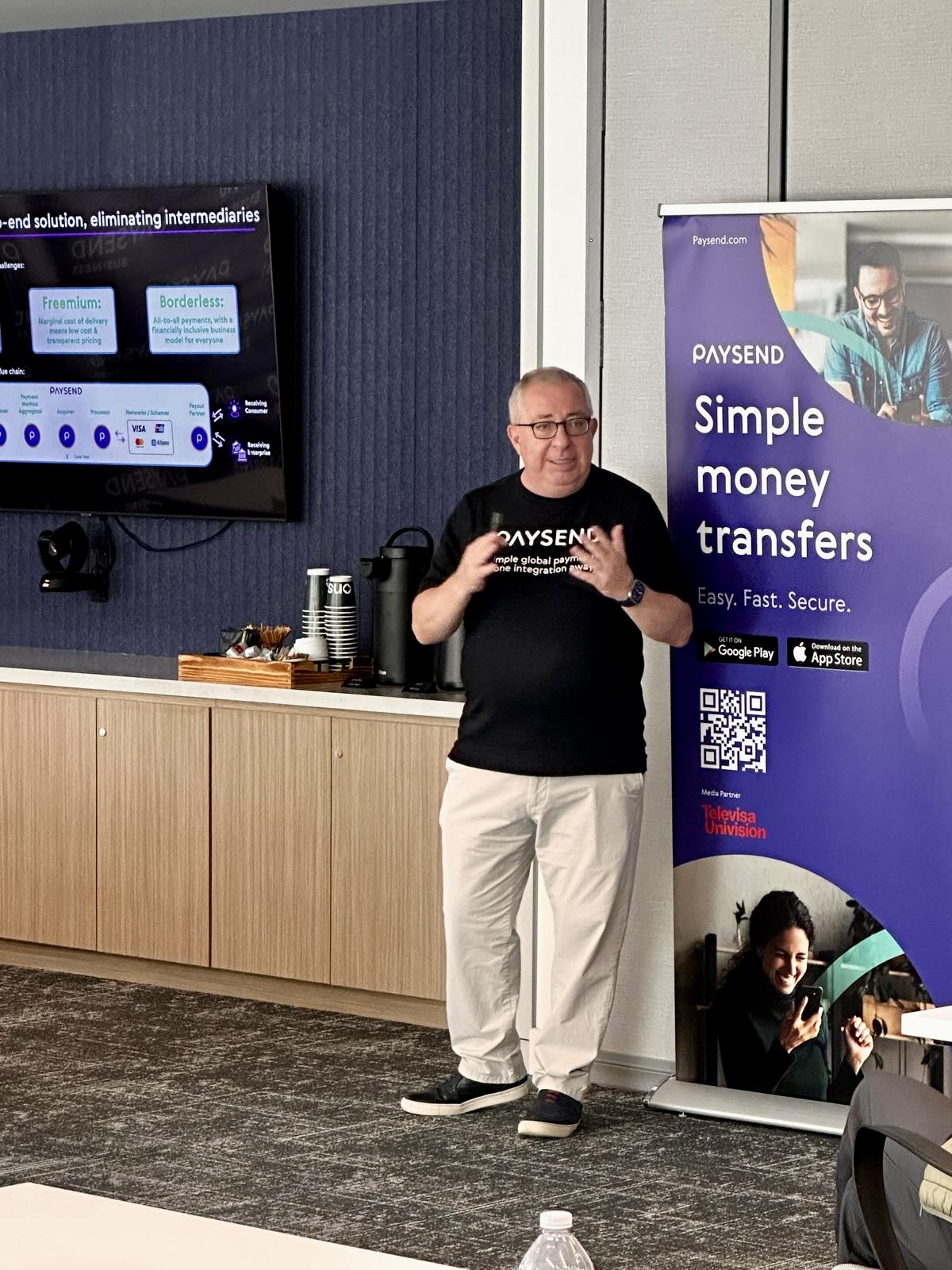 Man standing next to a purple banner that reads 'Simple money transfers' in a conference room.