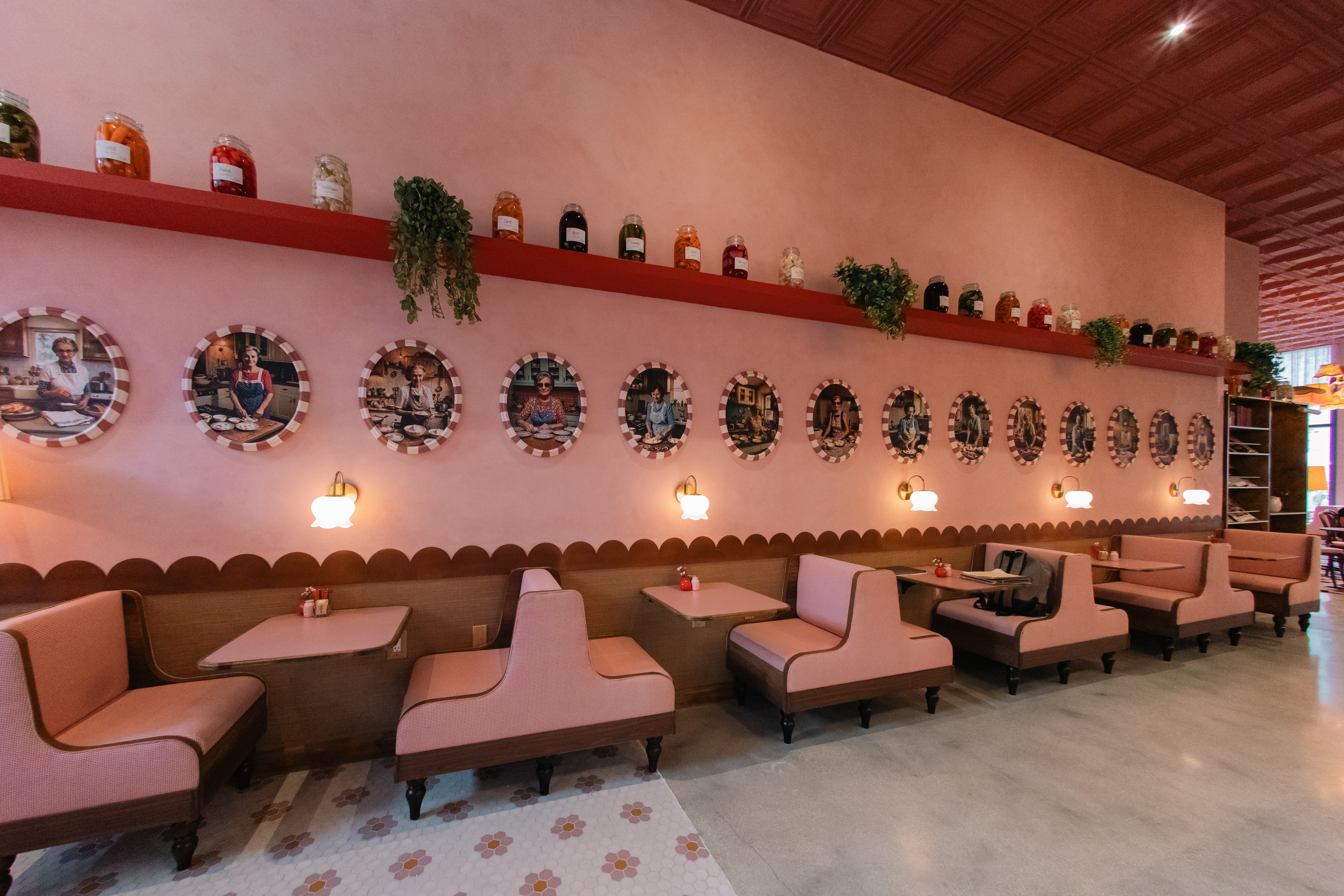 Interior of a cafe with pink walls, pink chairs, and a long pink bench, decorated with plants and circular art pieces.