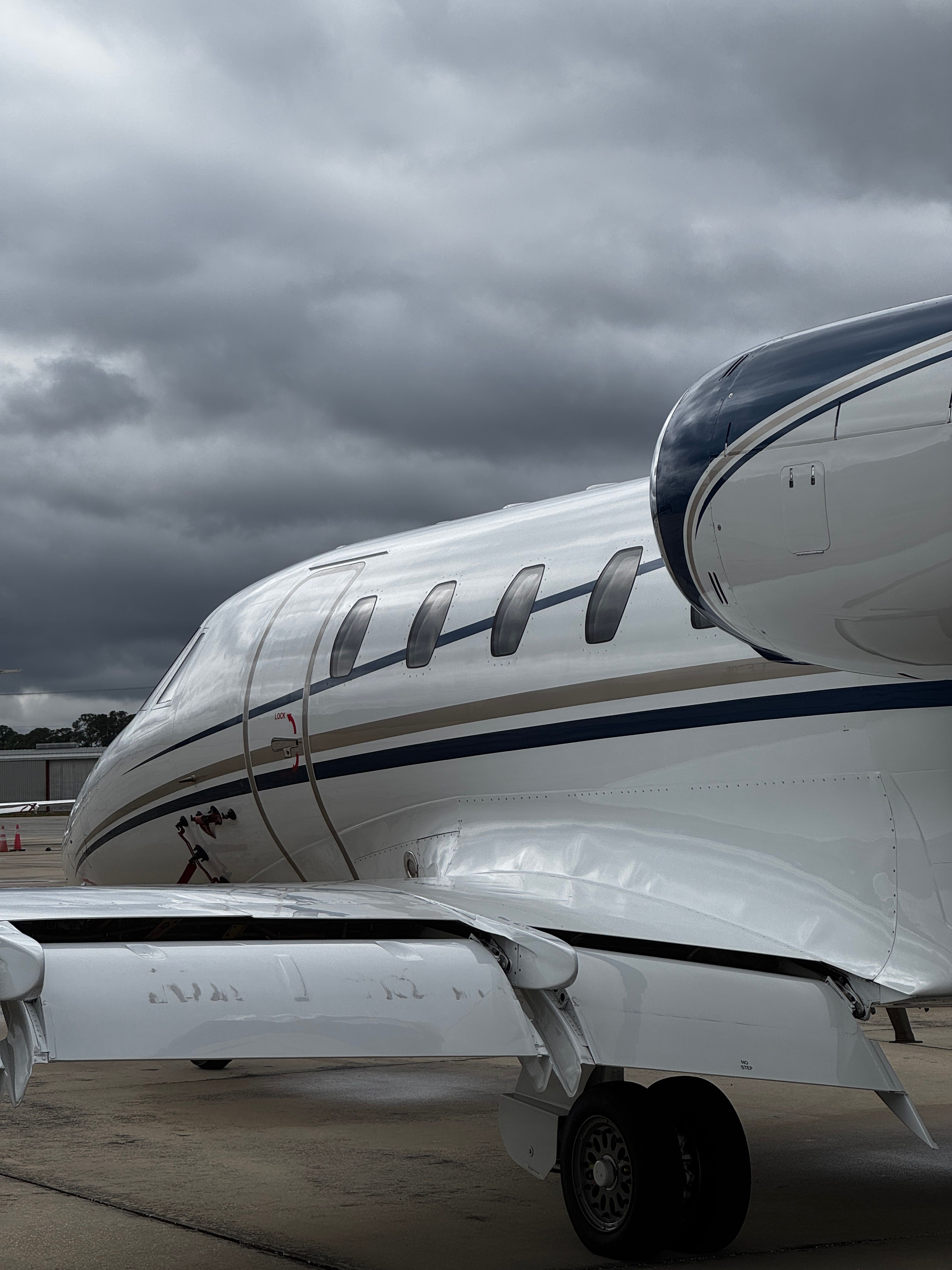Small white aircraft with blue stripe parked indoors, viewed from the side, with a closed door and a wheel visible.