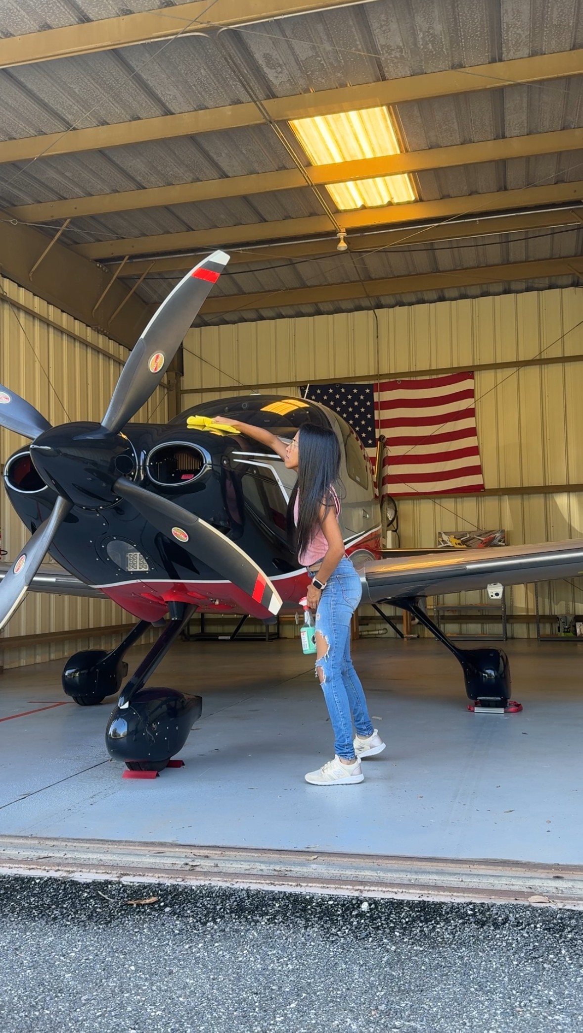 Person standing next to a small aircraft inside a hangar with an American flag on the wall.