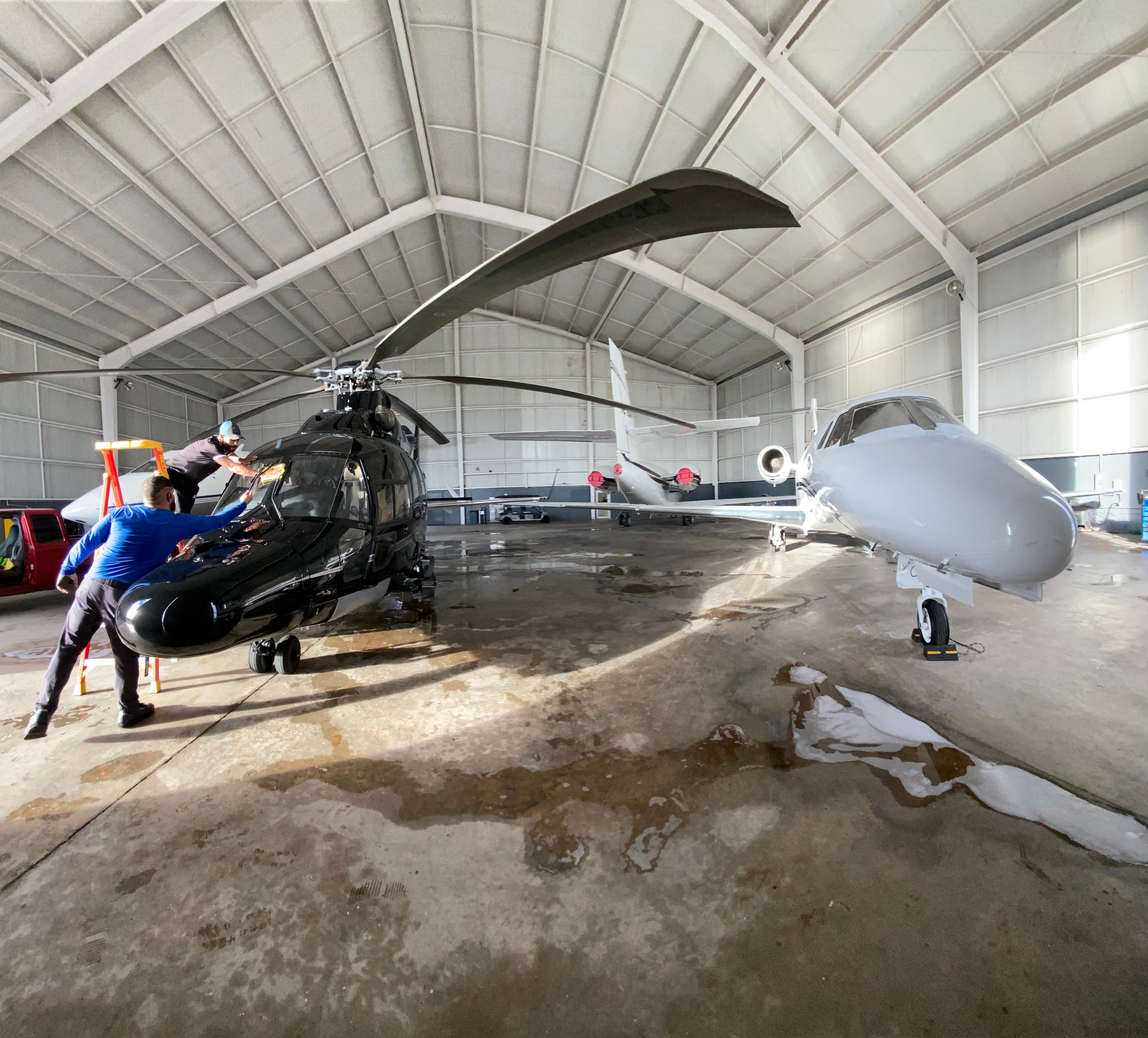 Two helicopters and a drone inside a hangar with a person near the helicopter on the left.