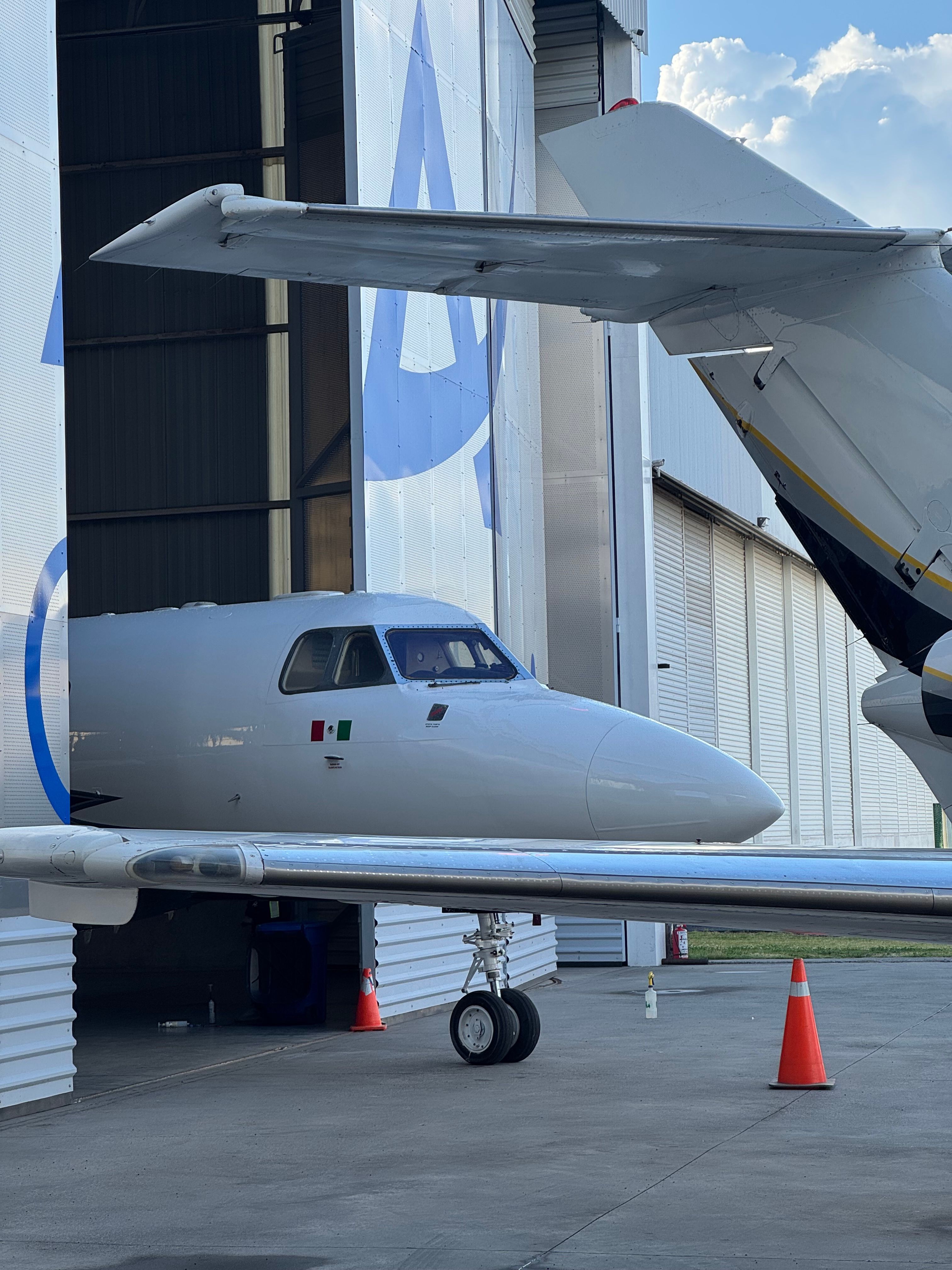 Small aircraft with open door parked outside near a building, with orange traffic cones on the ground.