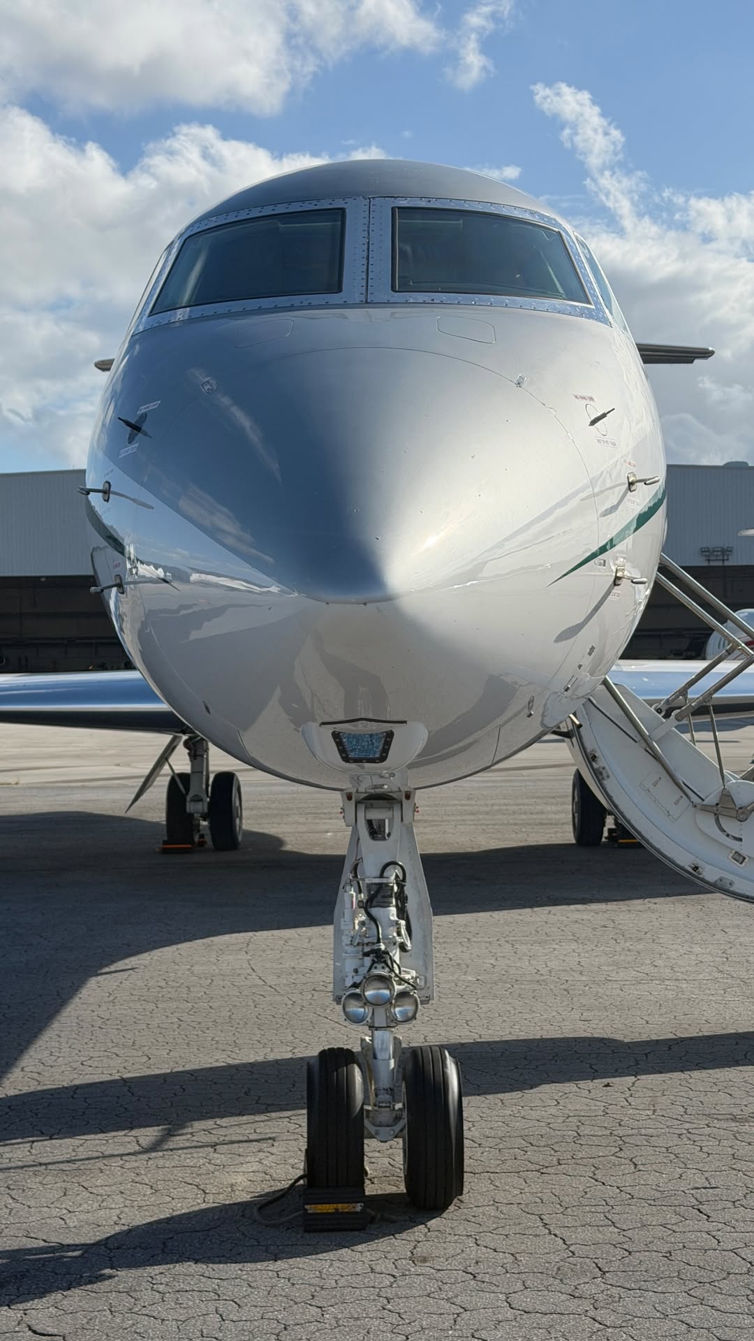 Front view of a large airplane on the tarmac with stairs on the side, under a partly cloudy sky.