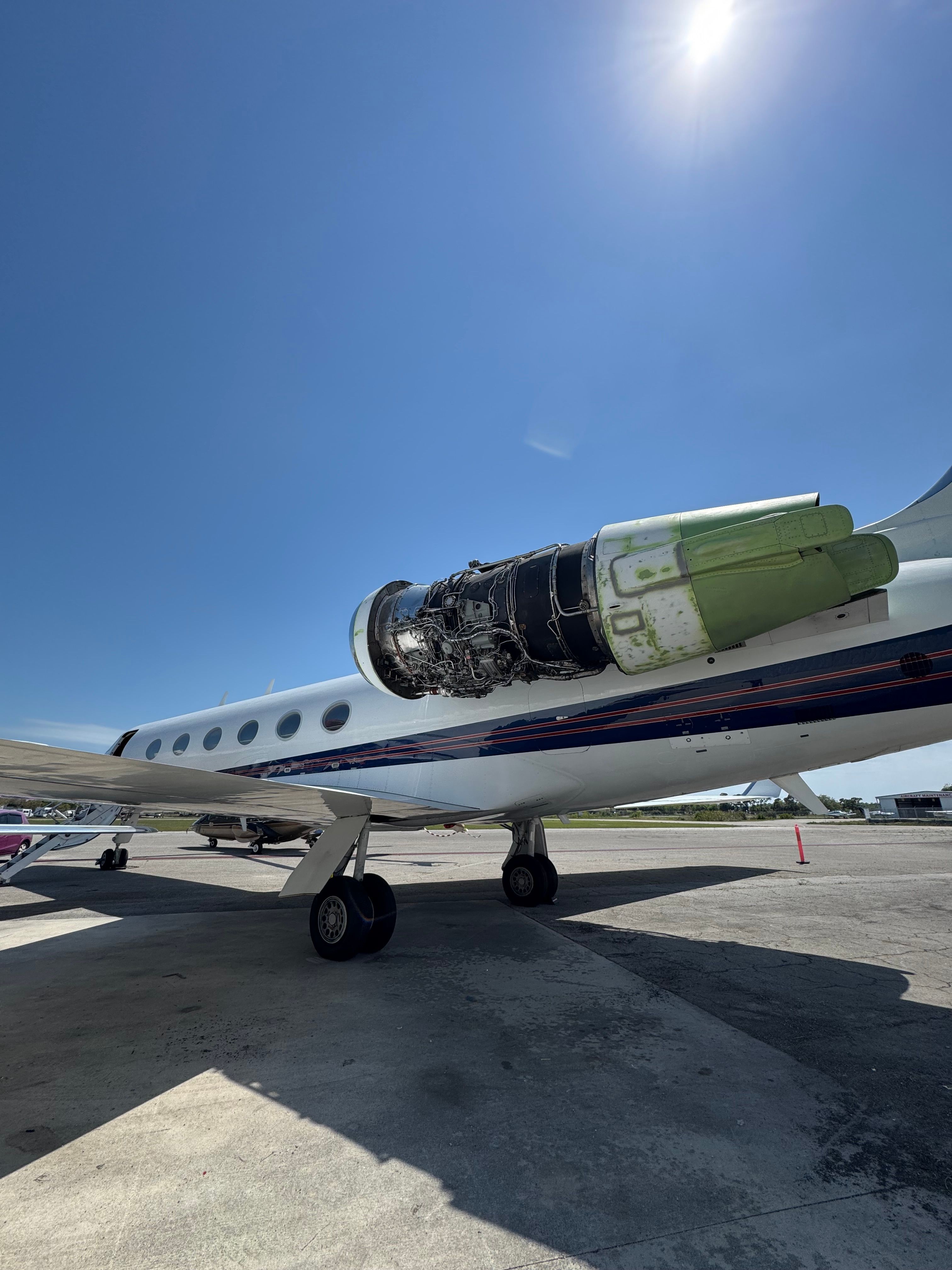 Small airplane parked on tarmac with clear blue sky and sun overhead.