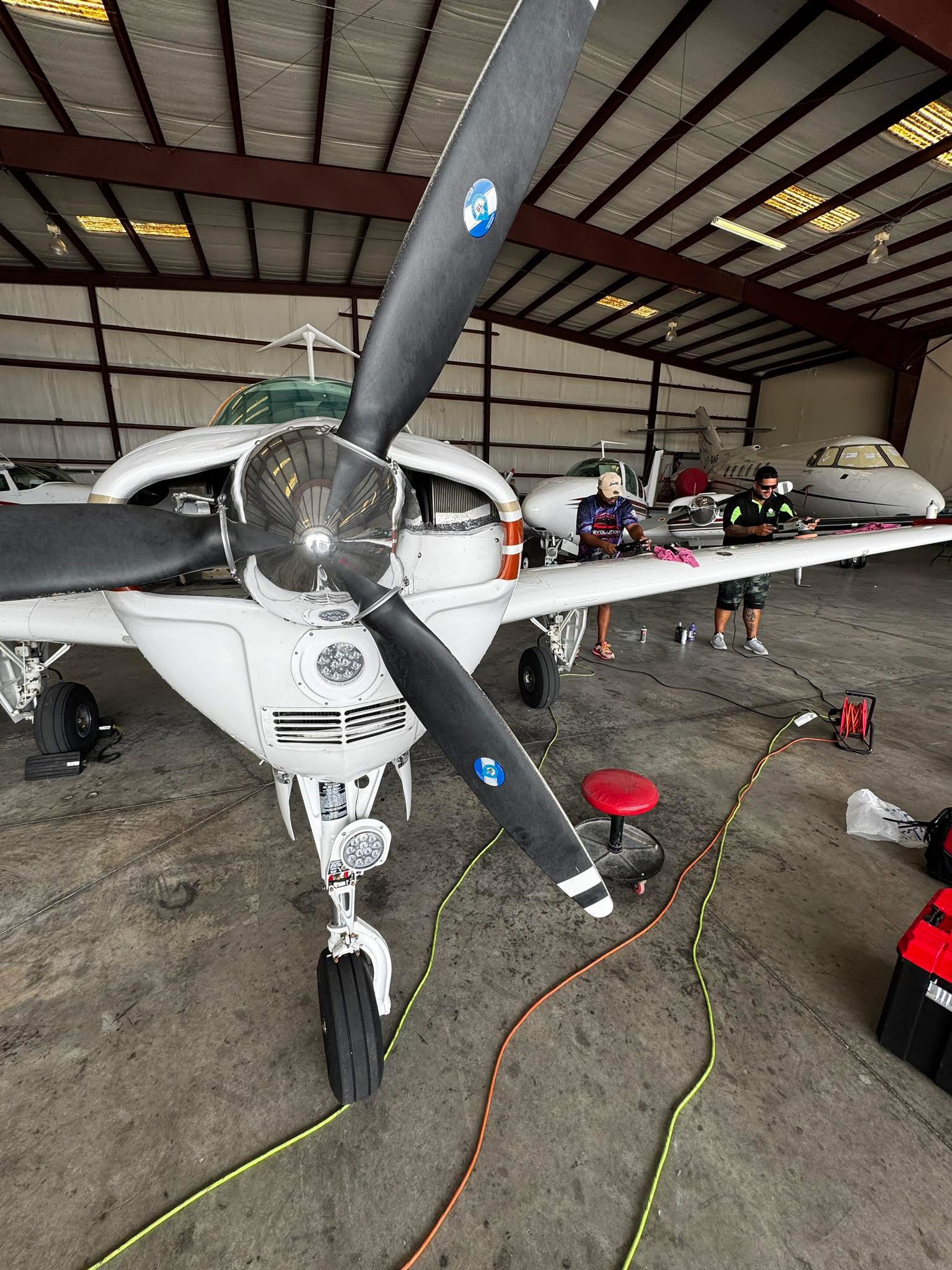 Propeller airplane inside a hangar with cars and people in the background.