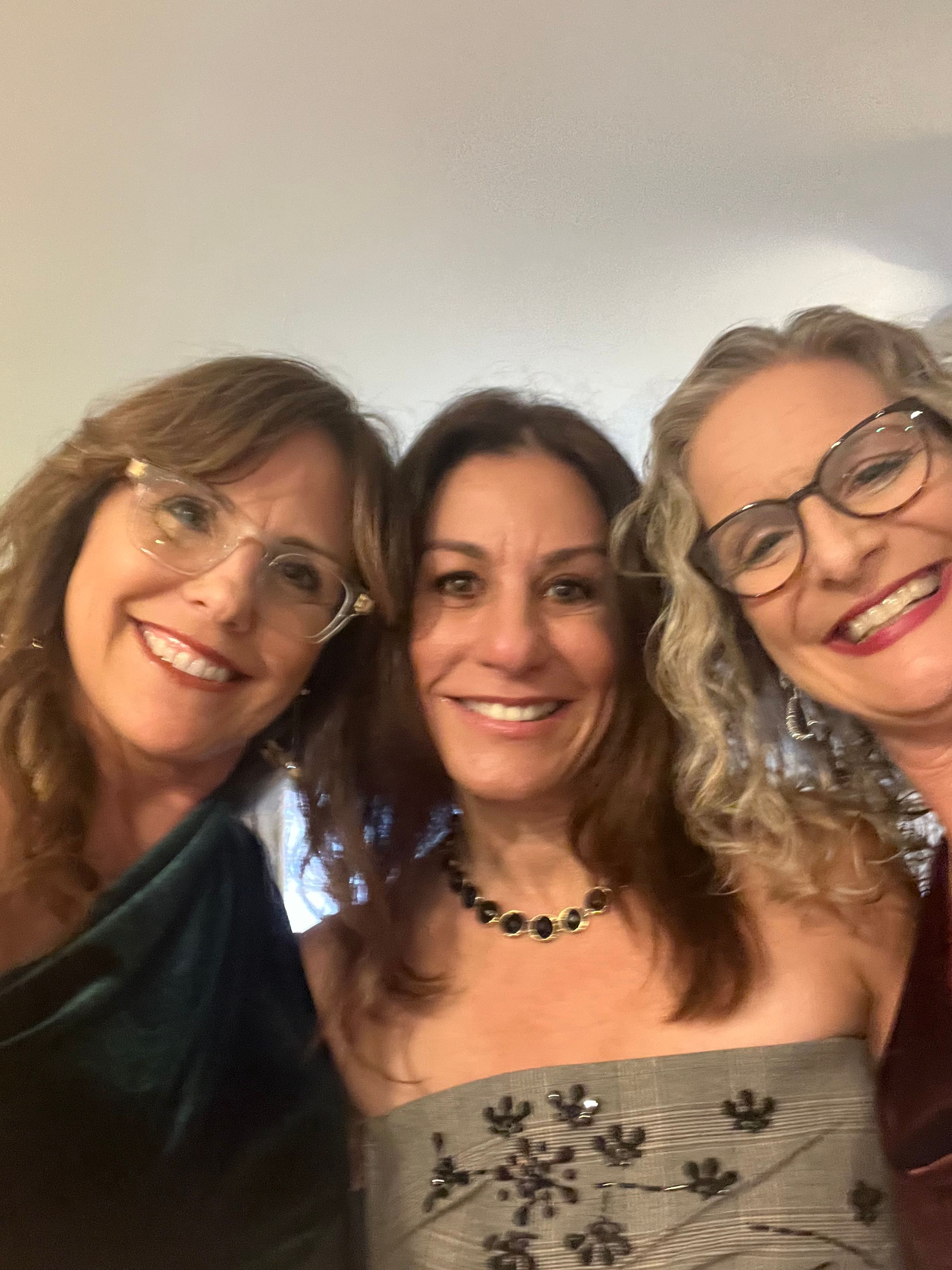 Three women smiling, one wearing glasses, in a close group photo.