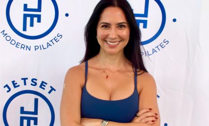 Woman with dark hair smiling, arms crossed, standing in front of Jetset Modern Pilates logo backdrop.