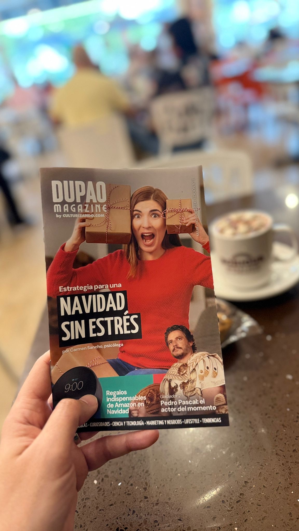 Hand holding a magazine titled 'DUPAO MAGAZINE' with a woman in a red shirt smiling, in a cafe setting.