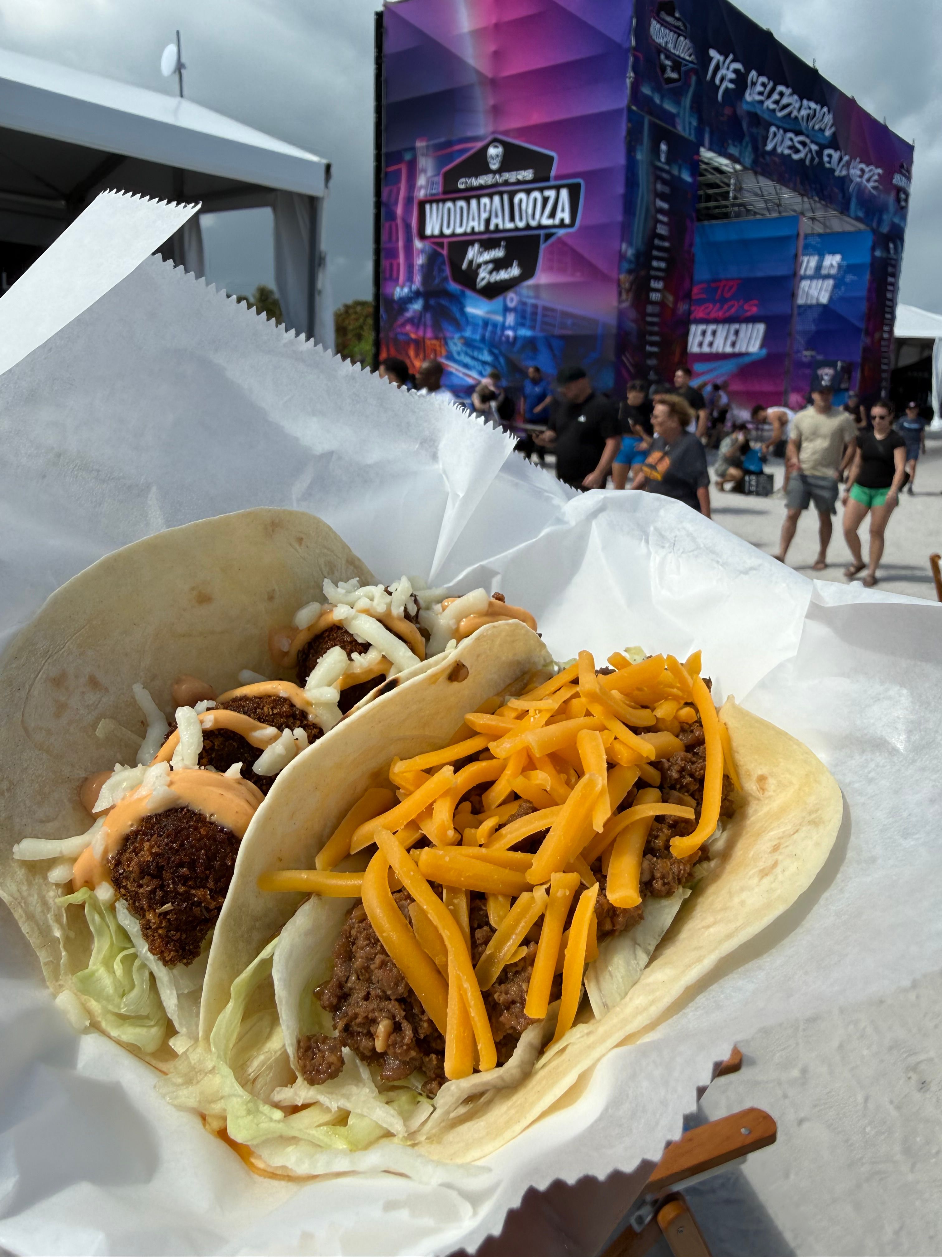 A taco with shredded cheese, lettuce, and meat in a soft tortilla, placed on white paper on a table.