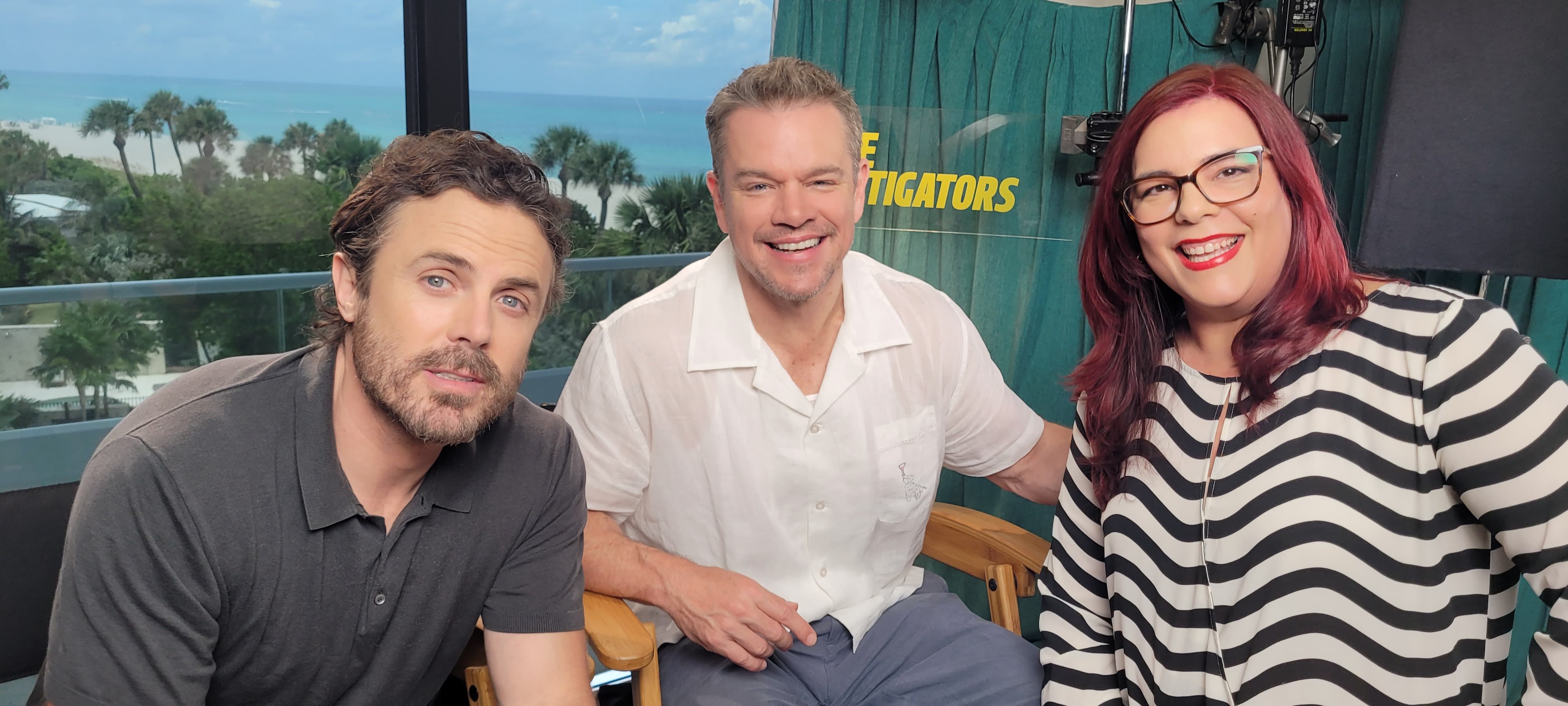 Three people sitting together, smiling, with a scenic outdoor background and a green curtain behind them.