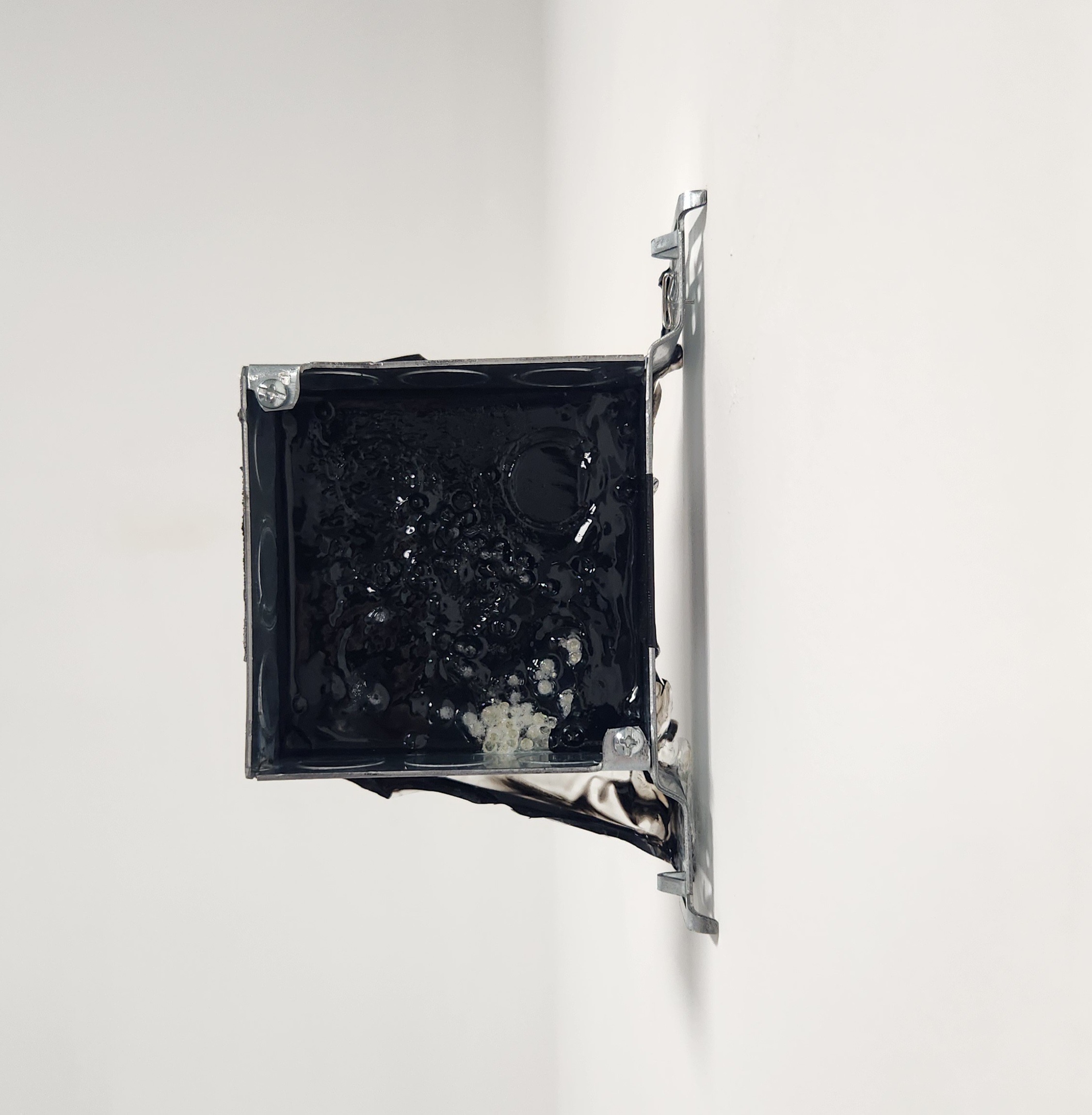 Electrical outlet with blackened interior mounted on a white wall, viewed from the side.