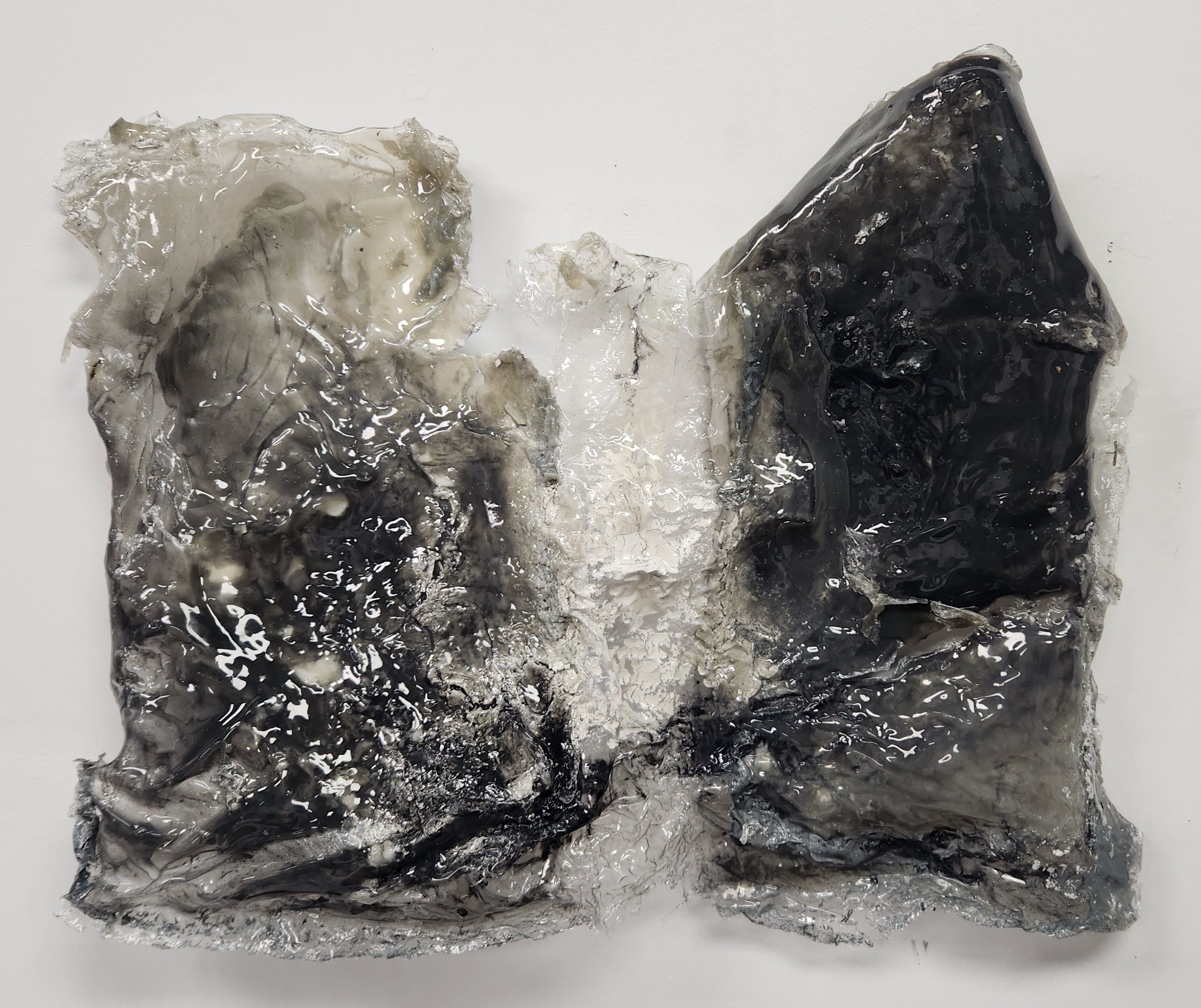 A piece of ice with black and white inclusions, irregular shape, and rough surface, on a white background.