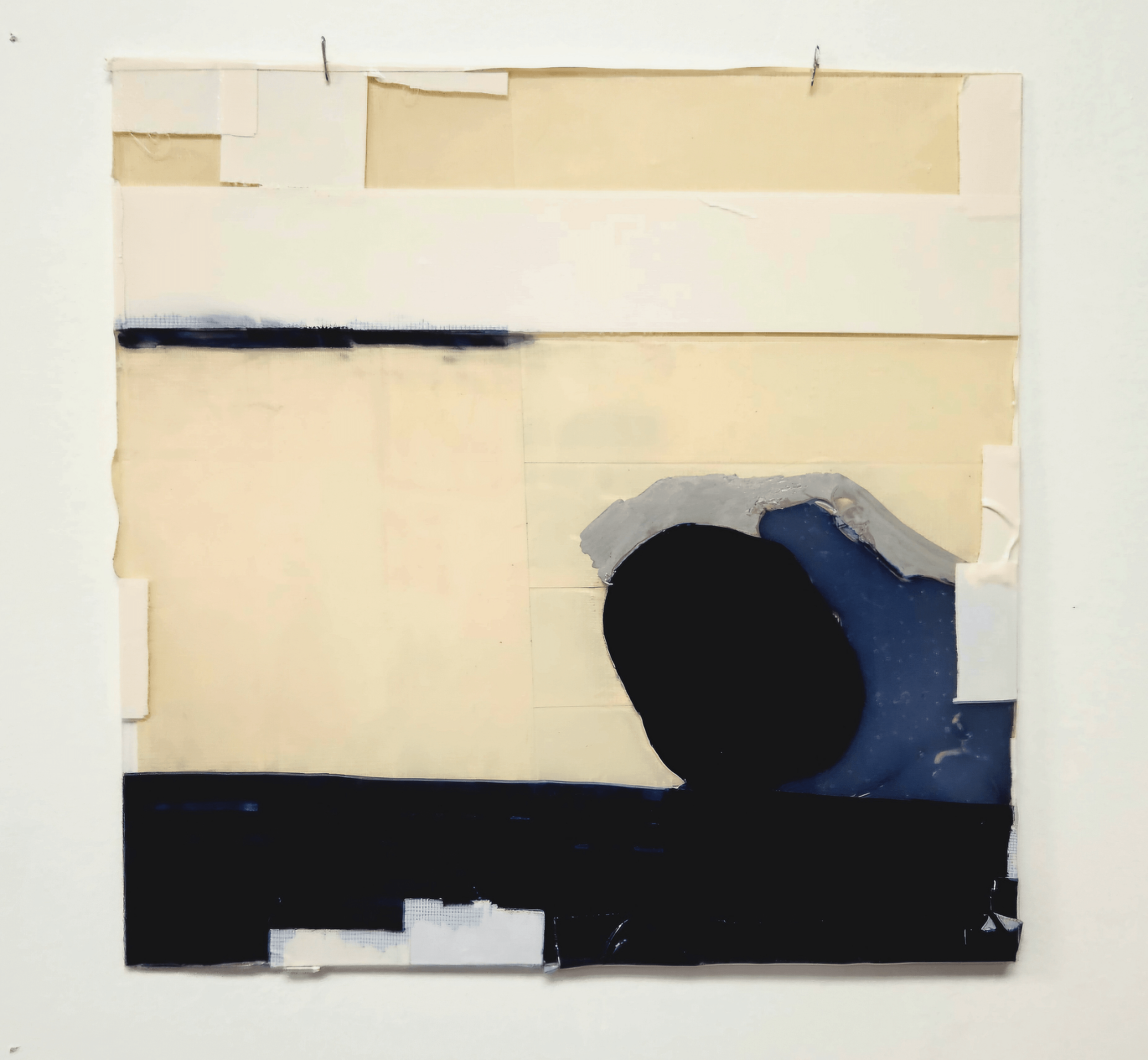 Abstract artwork with beige, white, black, and blue shapes, taped to a white wall.