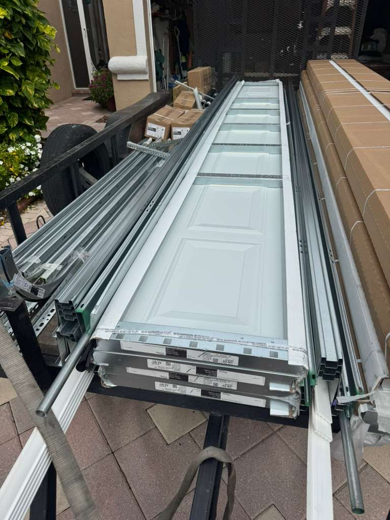 Stack of metal and glass door frames on a table outdoors, with plants and building elements in the background.