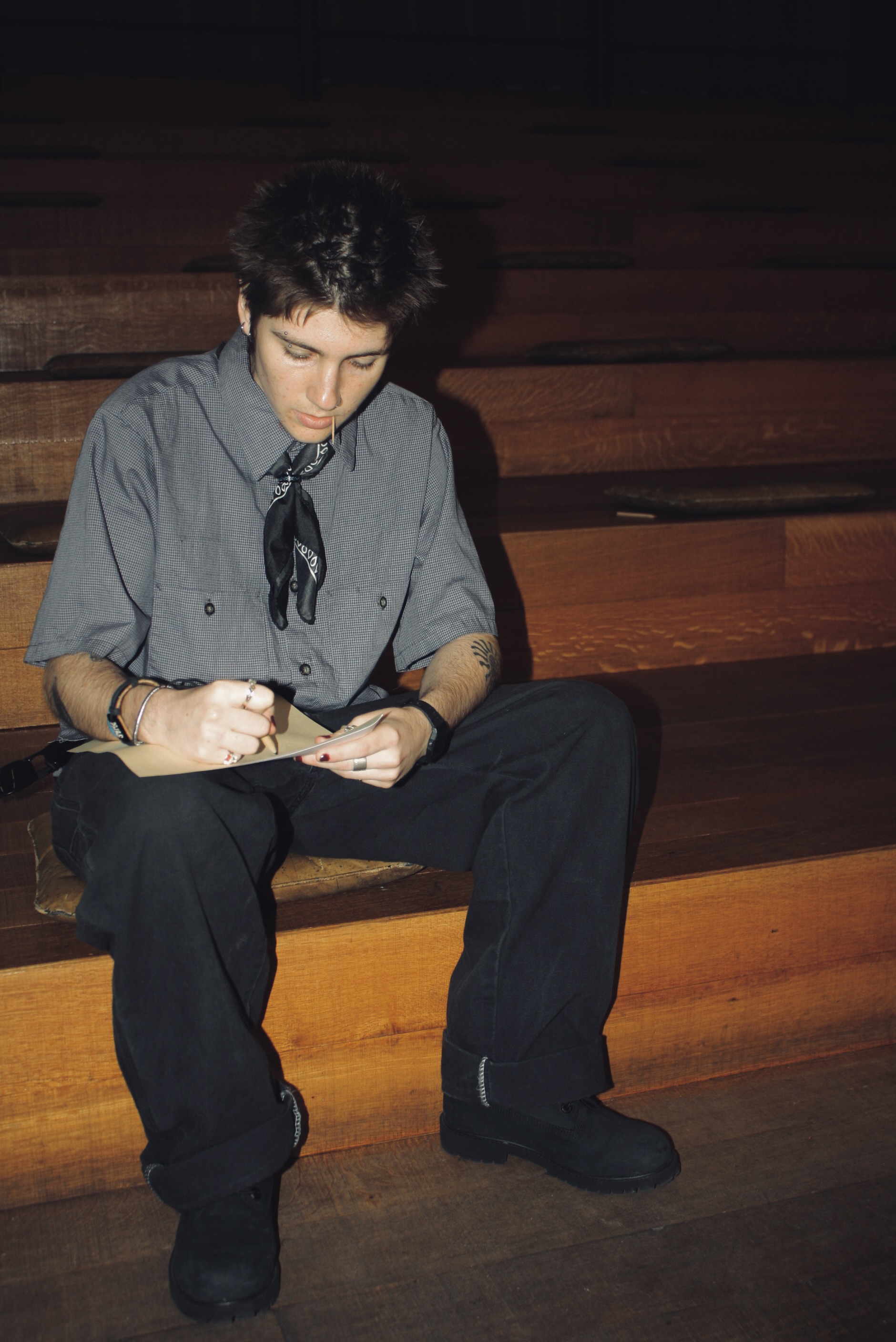 Person sitting on wooden steps, writing in a notebook, wearing a gray shirt and black pants.