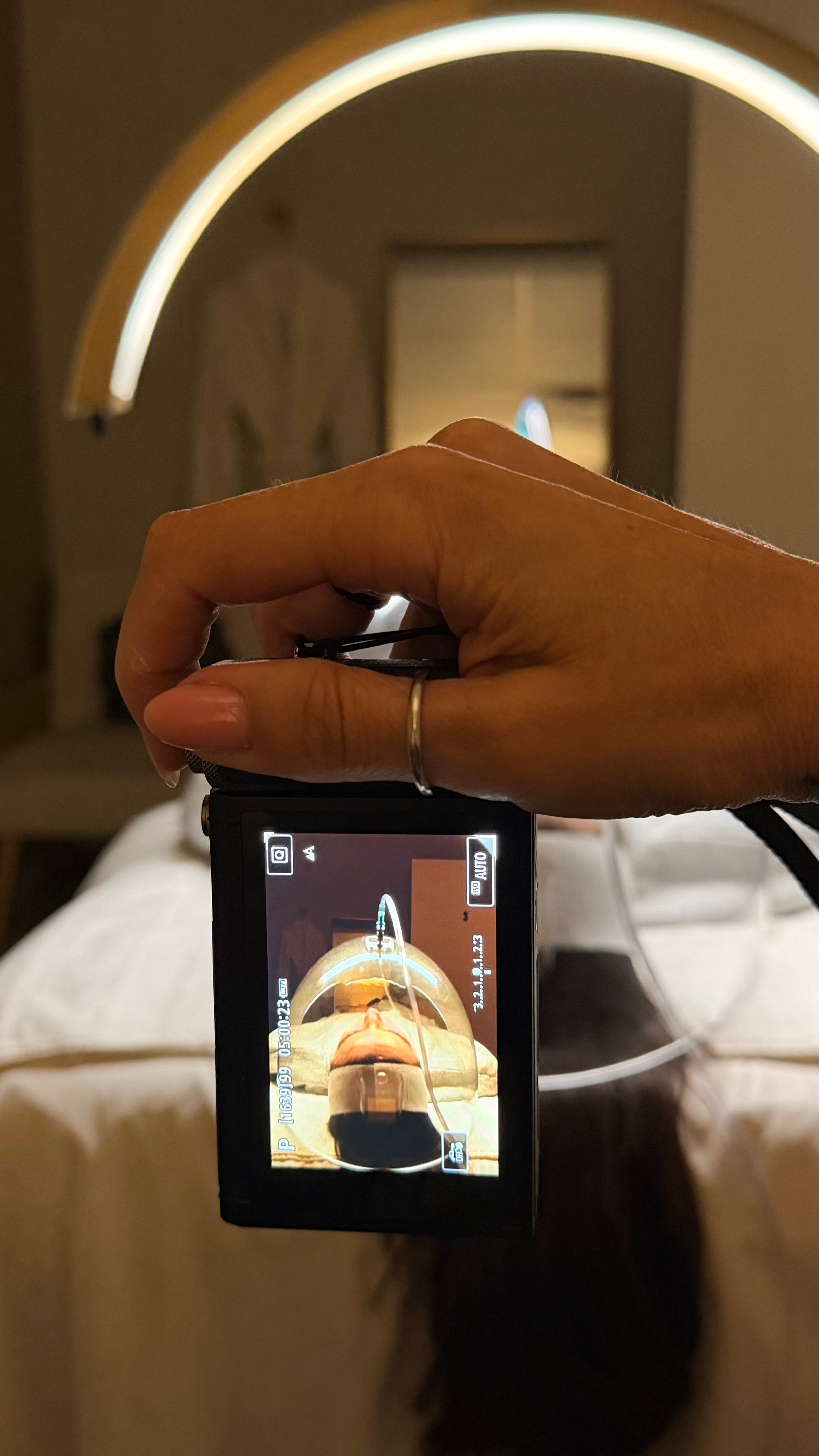 Person holding a camera taking a photo of their reflection in a mirror, with a circular light above.