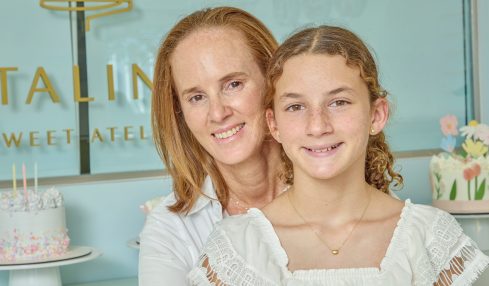 Two females smiling, one adult and one child, in front of a decorated cake and pastel background.